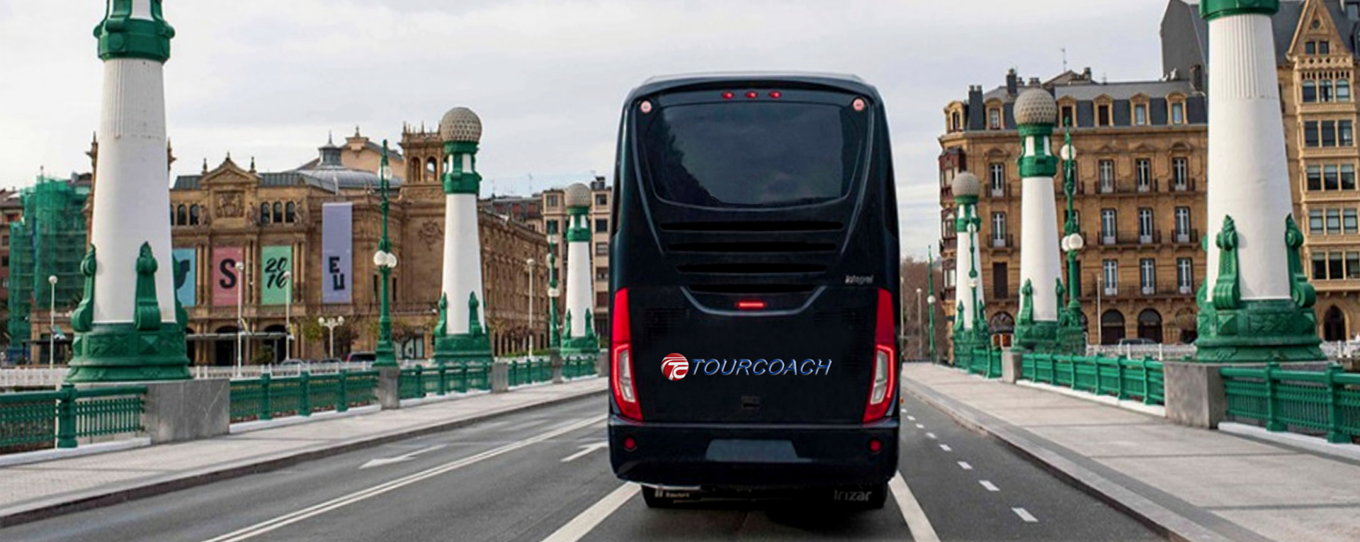 TourCoach Bus driving towards several large buildings
