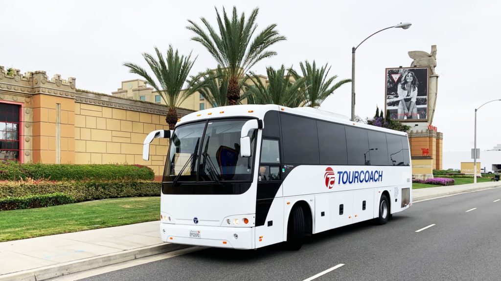 TourCoach bus driving down a road with palm trees